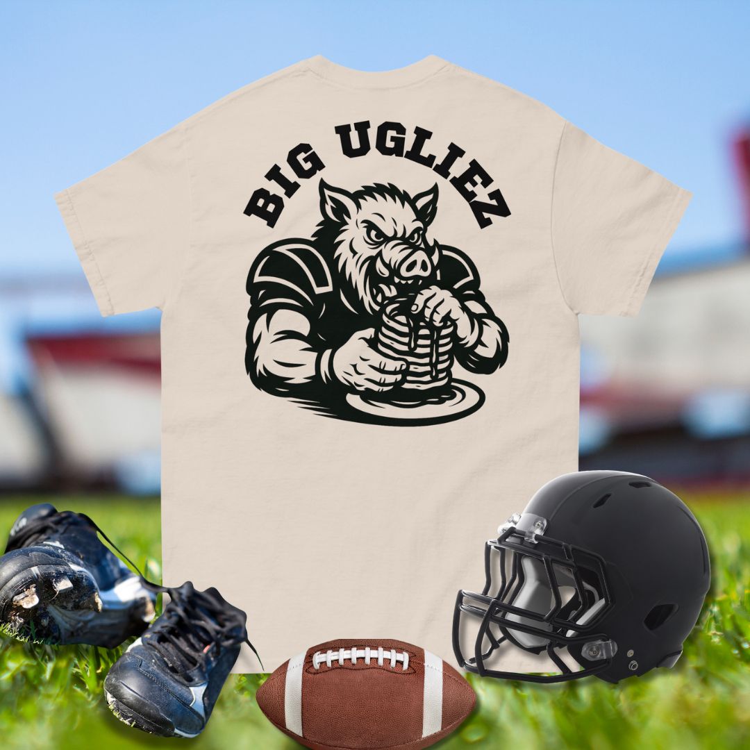 Beige t-shirt with 'BIG UGLIEZ' graphic, football helmet, cleats, and football on grass.