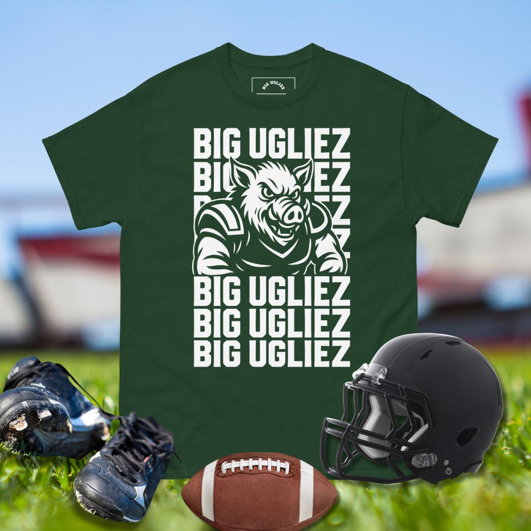 Green t-shirt with 'BIG UGLIEZ' graphic, football, helmet, and shoes on grass.