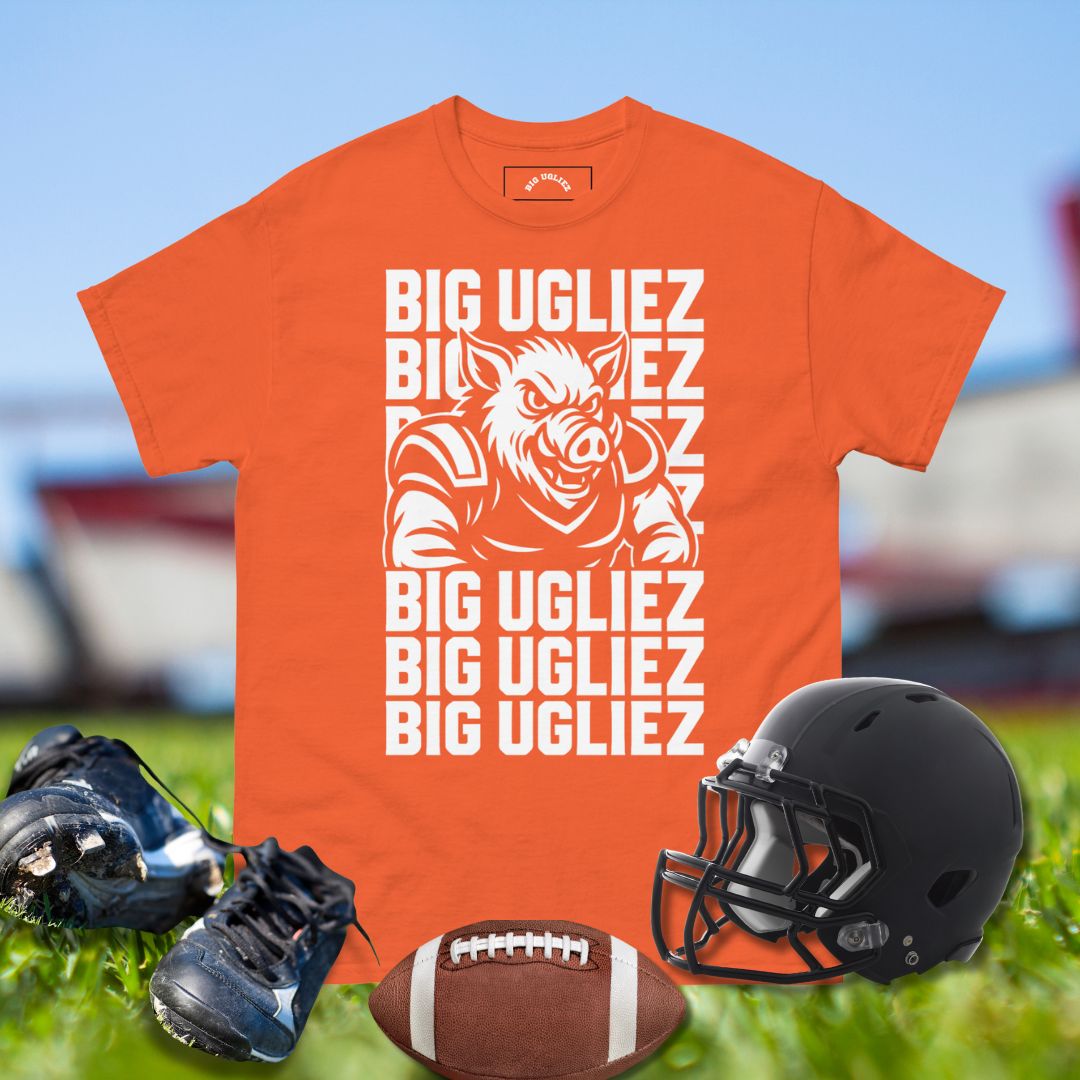 Orange t-shirt with 'BIG UGLIEZ' graphic, black football helmet, cleats, and football on grass.