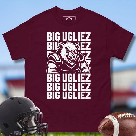 Maroon t-shirt with graphic design and text, helmet, and football on a blurred sports field background