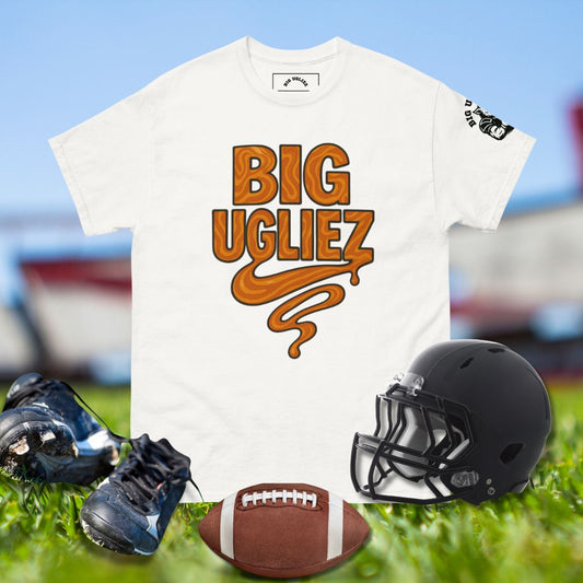 White t-shirt with 'BIG UGLIEZ' text, football helmet, cleats, and football on grass.