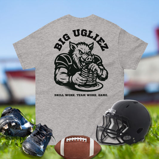 Gray t-shirt with 'Big Ugliez' graphic and football equipment on grass