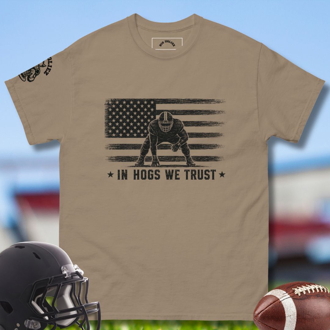 Beige t-shirt with football player graphic and 'In Hogs We Trust' text, helmet, and football on a sports-themed background.