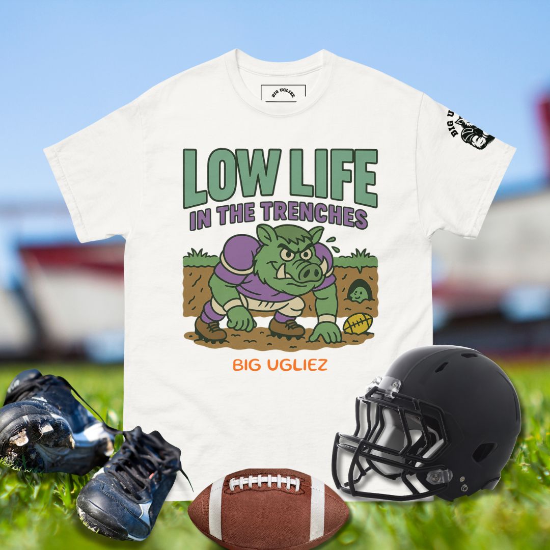 White t-shirt with cartoon pig graphic and text, black football helmet, cleats, and football on grass.