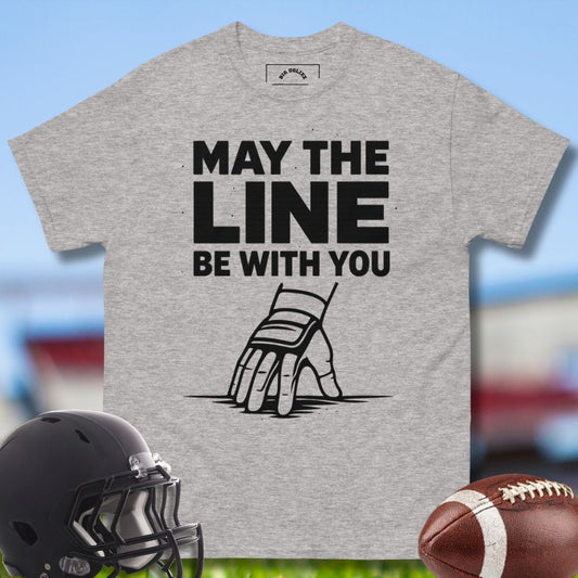 Gray t-shirt with 'May the Line Be With You' graphic and football helmet and ball on a sports field background