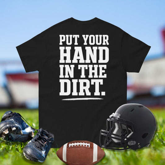 Black t-shirt with 'Put your hand in the dirt' text, football, helmet, and shoes on grass.
