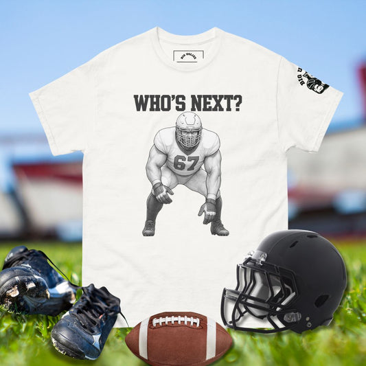 White t-shirt with football player graphic and 'WHO'S NEXT?' text, surrounded by football gear on a grassy field.