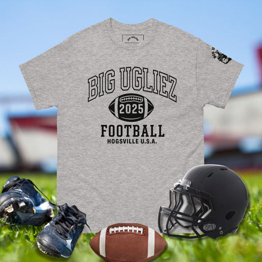 Gray t-shirt with 'BIG UGLIEZ 2025 FOOTBALL HOGGVILLE U.S.A.' text, black helmet, football, and cleats on grass.