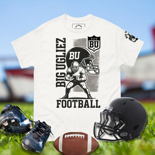White t-shirt with football-themed design, black helmet, football, and cleats on a grassy field background.