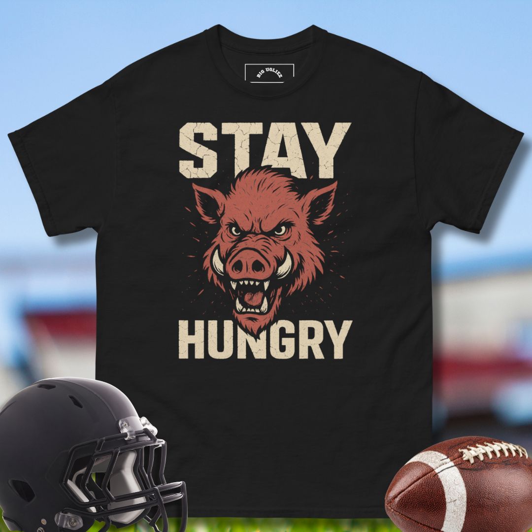 Black t-shirt with a graphic of a hog and 'Stay Hungry' text, helmet, and football on a sports field background.