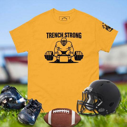 Yellow t-shirt with 'Trench Strong' graphic, football, helmet, and cleats on grass.