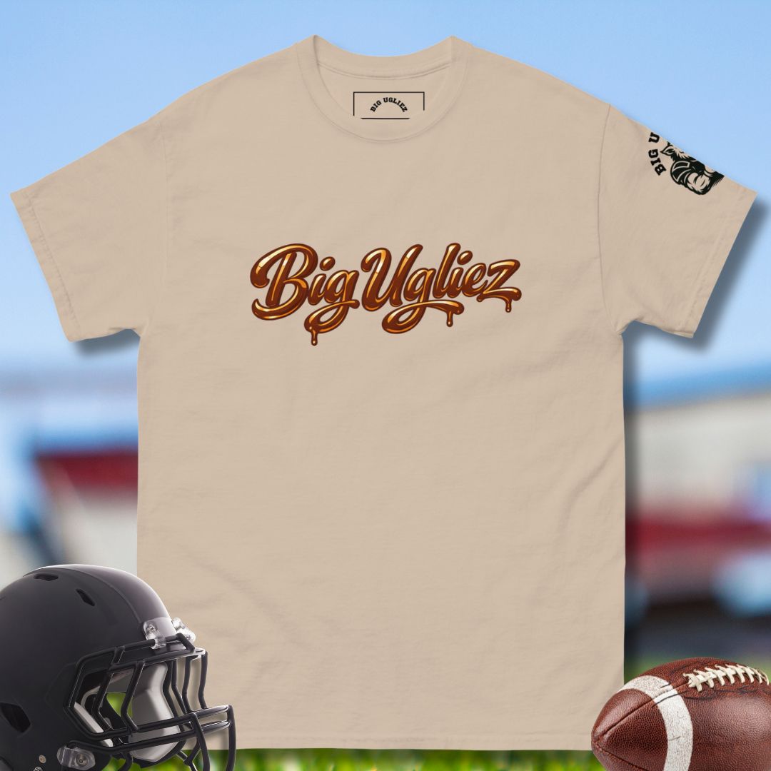 Beige t-shirt with 'Big Uglyz' text, black football helmet, and brown football on a blurred sports field background.