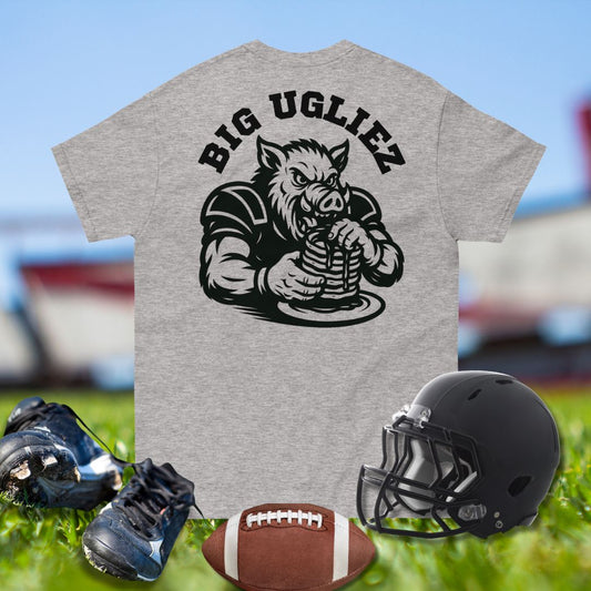 Gray t-shirt with a graphic of a pig and 'BIG UGLIEZ' text, paired with football gear on grass.