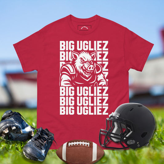 Red t-shirt with 'BIG UGLIEZ' text and pig graphic, black football helmet, cleats, and football on grass.
