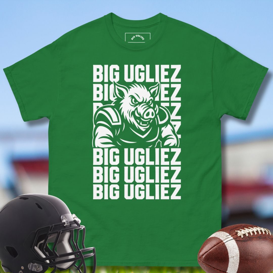 Green t-shirt with 'BIG UGLIEZ' graphic and football helmet and ball on a blurred sports field background