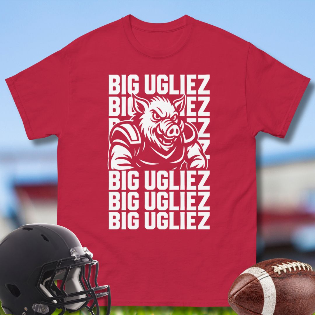 Red t-shirt with a graphic and text 'BIG UGLIEZ' on a blurred sports field background.