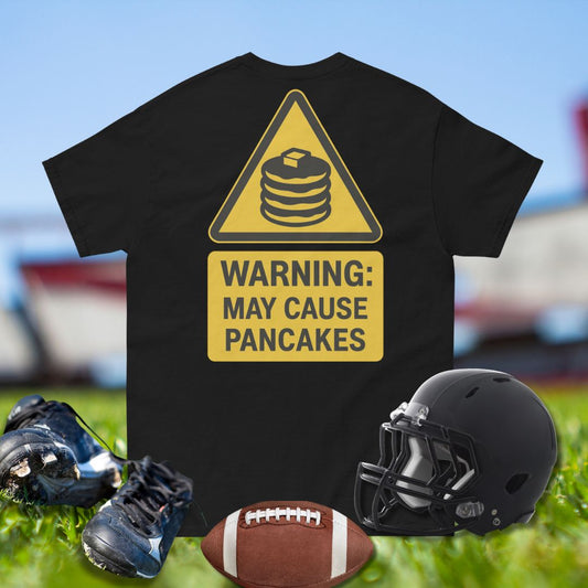 Black t-shirt with yellow warning sign graphic on grass with football, shoes, and helmet.