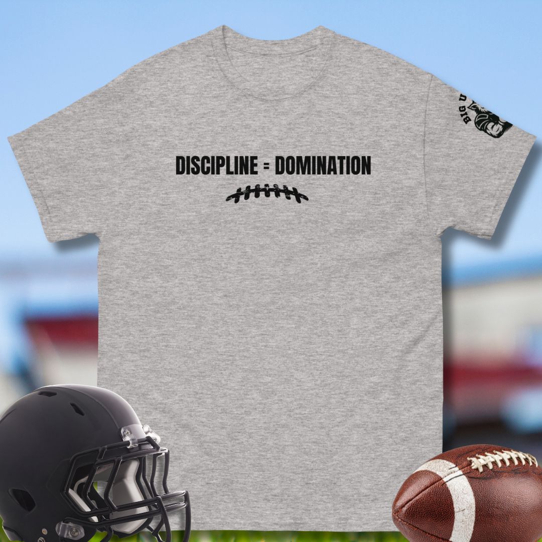 Gray t-shirt with 'Discipline = Domination' text, black football helmet, and brown football on a blurred sports field background. 