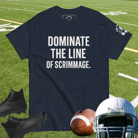 Navy t-shirt with 'Dominate the Line of Scrimmage' text on a grass field background, with football gear below.
