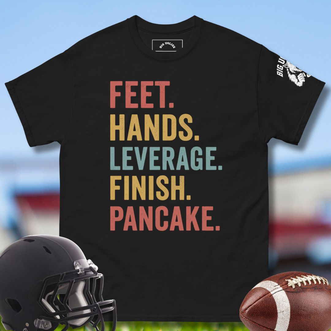 Black t-shirt with colorful text and football equipment on a blurred sports field background, Feet_hands leverage finish pancake olineman tshirt in black