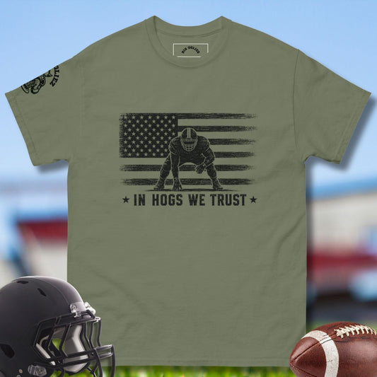 Green t-shirt with American flag and football player graphic, helmet, and football on a blurred sports field background.