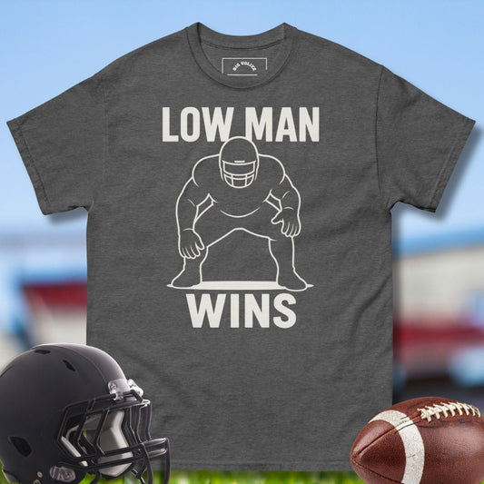 Gray t-shirt with 'LOW MAN WINS' graphic, football helmet, and football on a sports field background