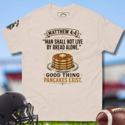 Beige t-shirt with pancake graphic and text, helmet, and football on a blurred sports field background