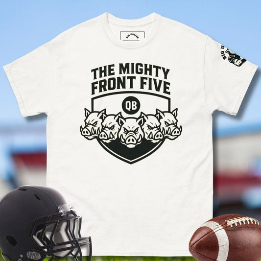 White t-shirt with 'The Mighty Front Five' design, black football helmet, and brown football on a blurred sports field background.