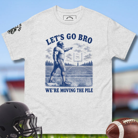 Gray t-shirt with football graphic and text 'Let's Go Bro, We're Moving the Pile' on a blurred sports background.