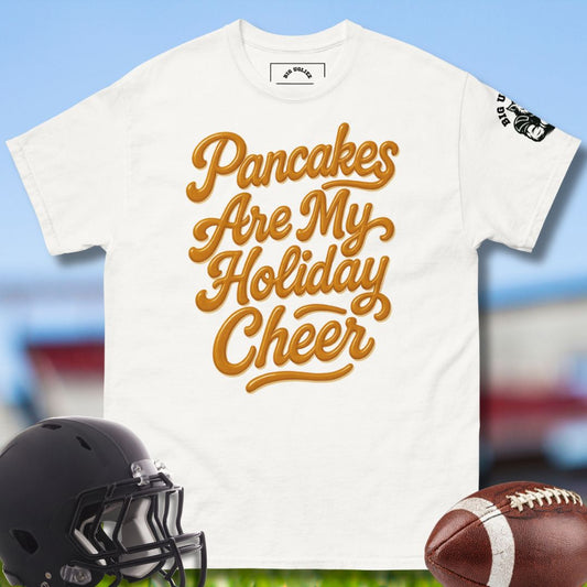 White t-shirt with 'Pancakes Are My Holiday Cheer' text, football, and helmet on a blurred sports field background