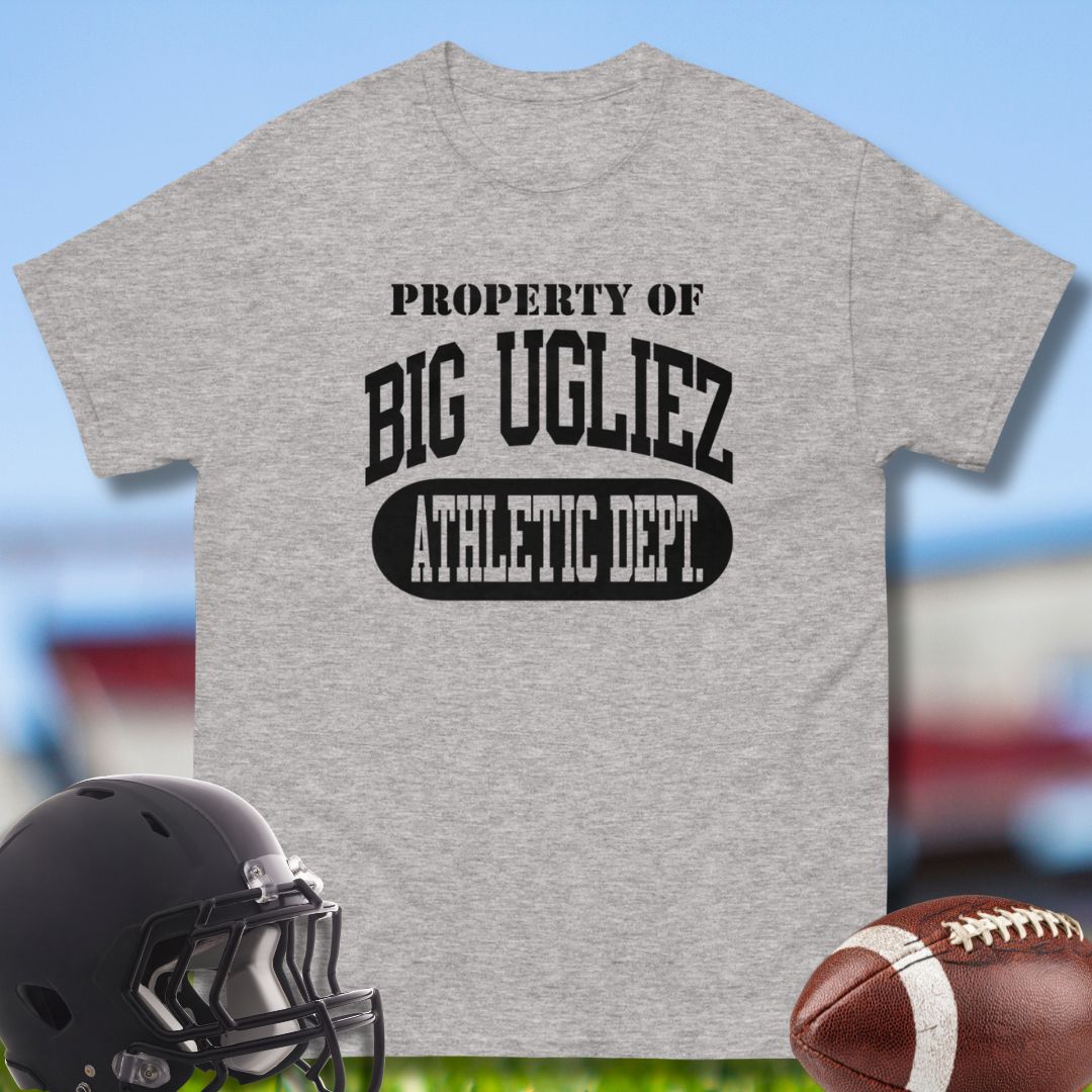 Gray t-shirt with 'Property of Big Ugliez Athletic Dept.' text, helmet, and football on a sports field background