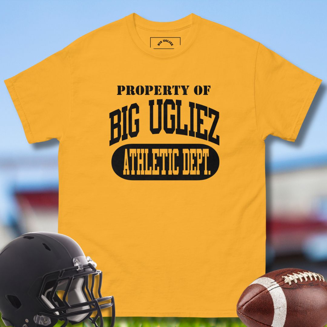 Yellow t-shirt with 'Property of Big Ugliez Athletic Dept.' text, black helmet, and football on a blurred sports field background.