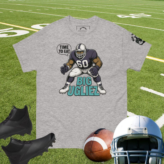 Gray t-shirt with football player graphic on grass field, surrounded by football gear.