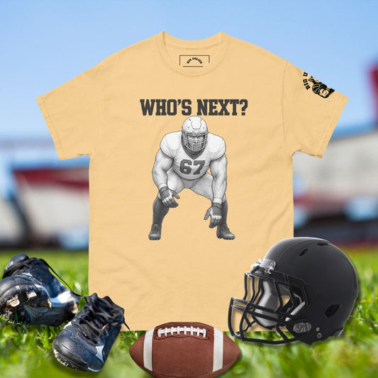 Beige t-shirt with football player graphic and 'WHO'S NEXT?' text, surrounded by football gear on a sports field background.