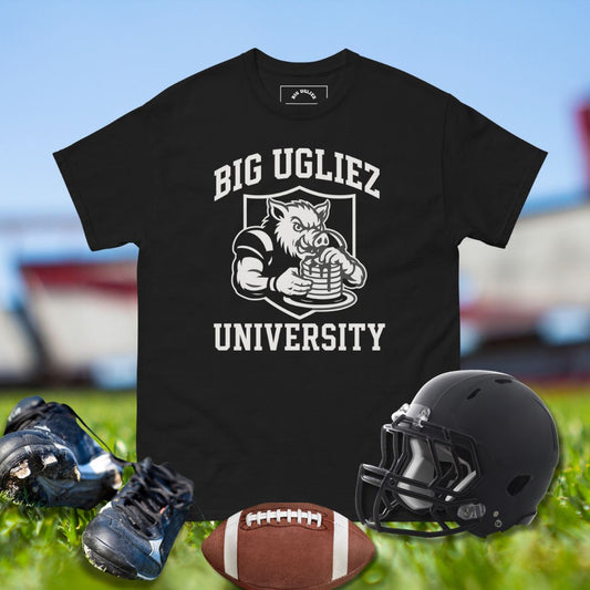 Black t-shirt with 'BIG UGLIEZ UNIVERSITY' graphic, football, helmet, and shoes on grass.