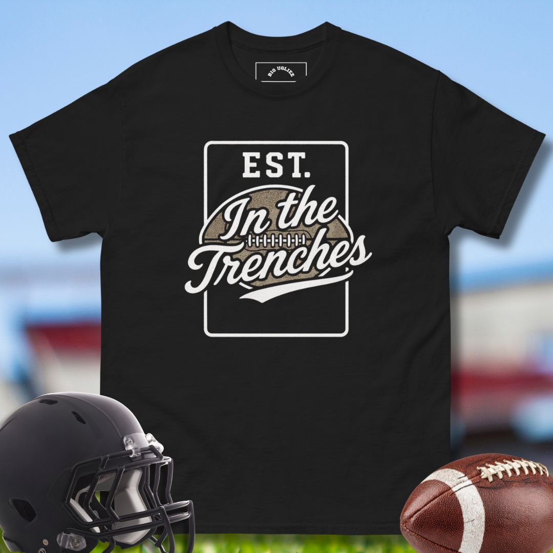 Black t-shirt with 'In the Trenches' design, football helmet, and football on a sports field background
