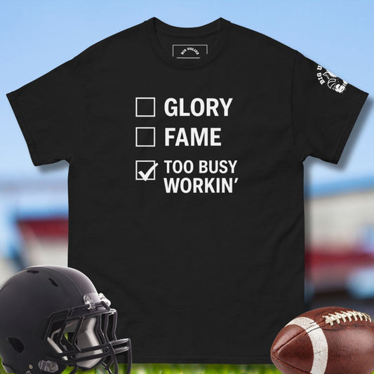 Black t-shirt with text 'GLORY, FAME, TOO BUSY WORKIN'' on a sports-themed background with helmet and football. For the football onlineman